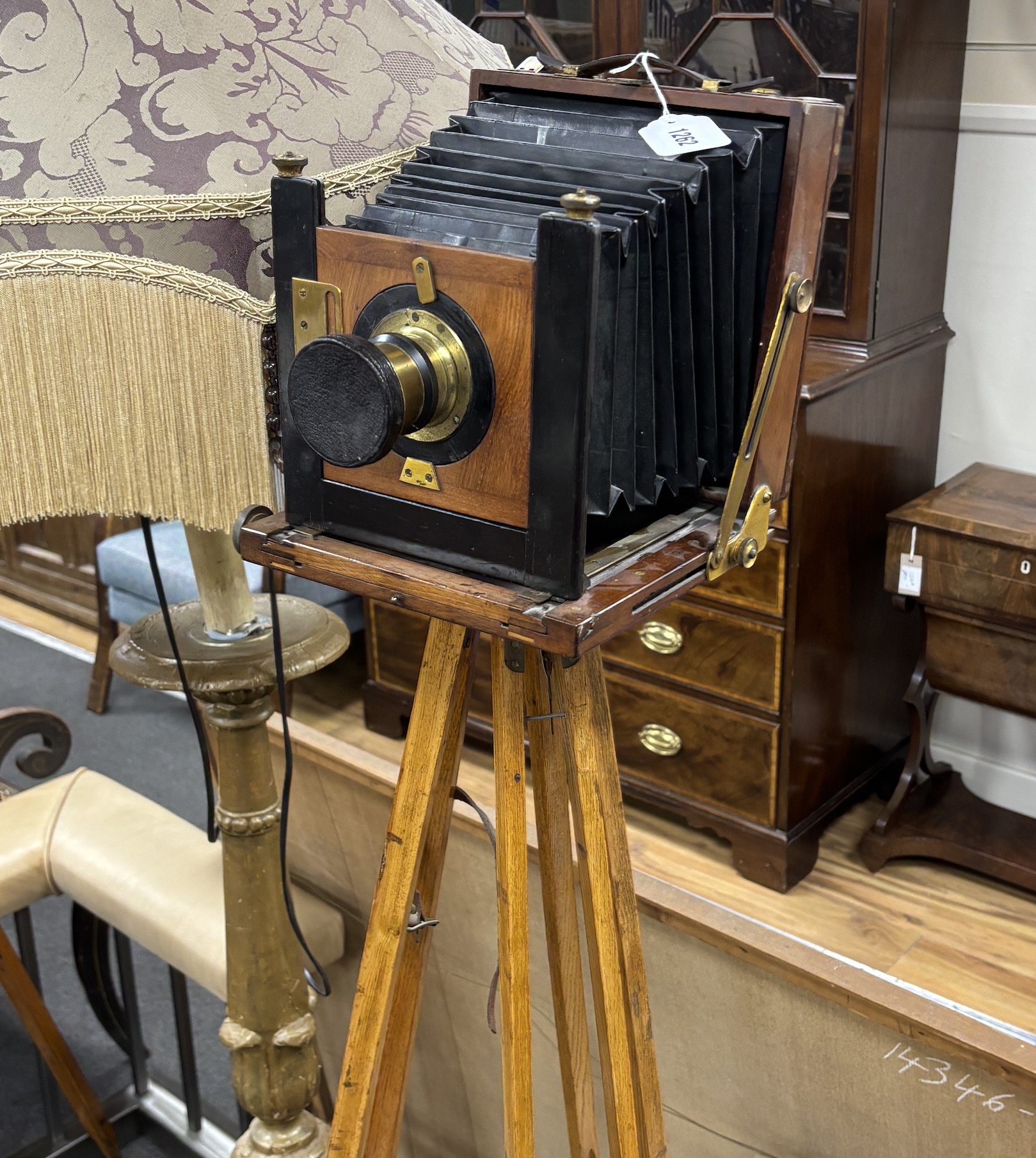 An early 20th century brass and mahogany ‘Challenge’ half plate bellows camera by J. Lizars, Glasgow, with a lens, and on an oak tripod